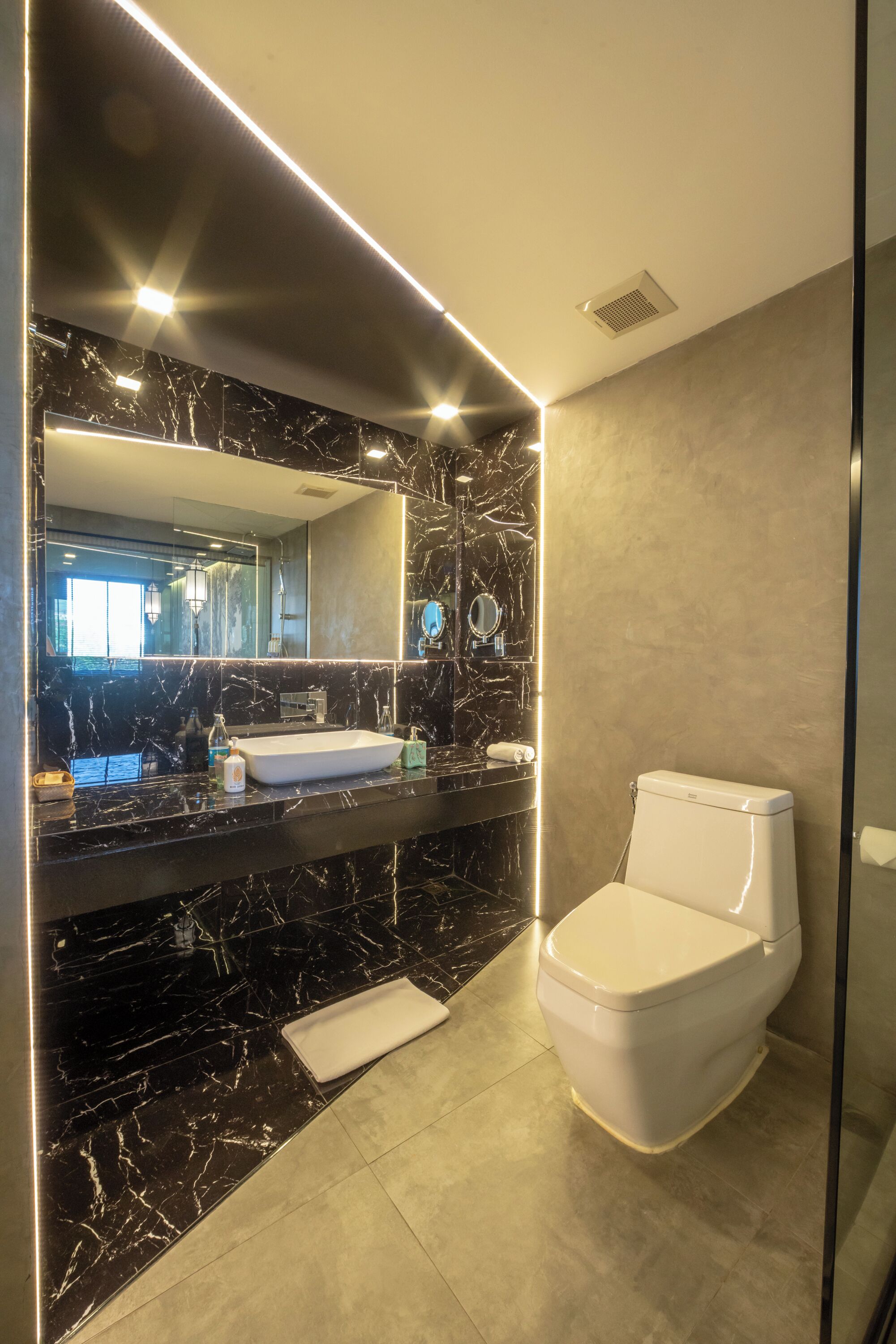 A modern bathroom with a marble vanity, a toilet, and a large mirror.