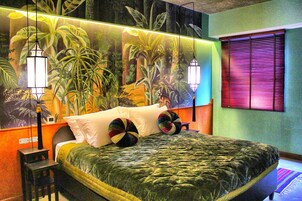 A bedroom with a large bed, a mural of a forest, and a window with blinds.