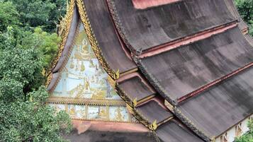Ein traditioneller Tempel mit gestuften Dächern und aufwendigen, goldenen Verzierungen, umgeben von üppigem Grün.