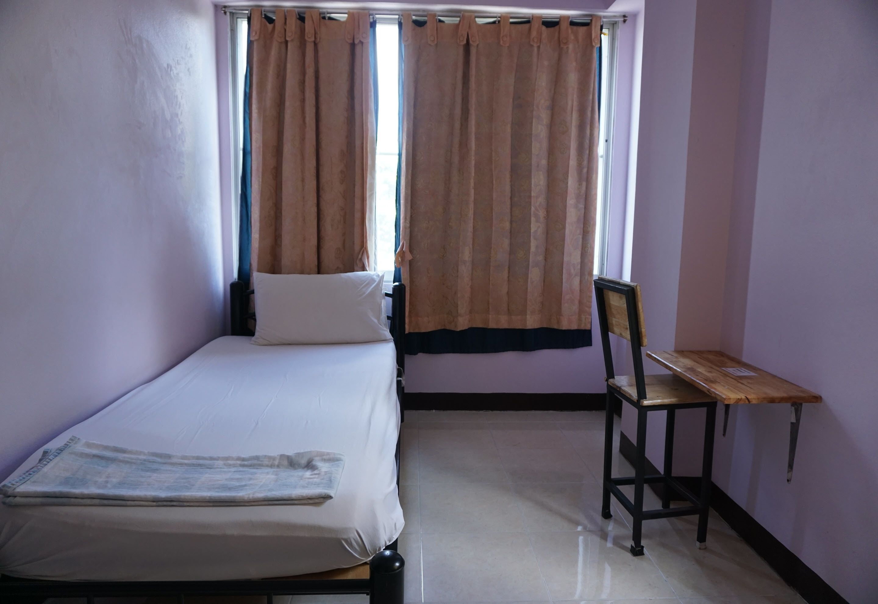 A single bed with a white mattress and a wooden chair with a small table beside it.