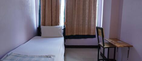 A single bed with a white mattress and a wooden chair with a small table beside it.