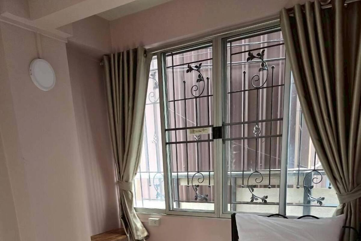 A bedroom with a bed, a window with metal bars, a curtain, and a small shelf.