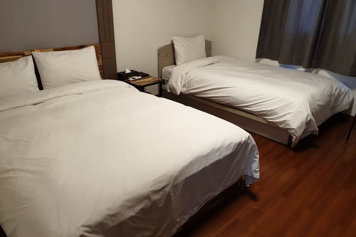 Ett hotellrum med två separata sängar, trägolv, ett nattduksbord med en lampa och ett fönster med gardiner.