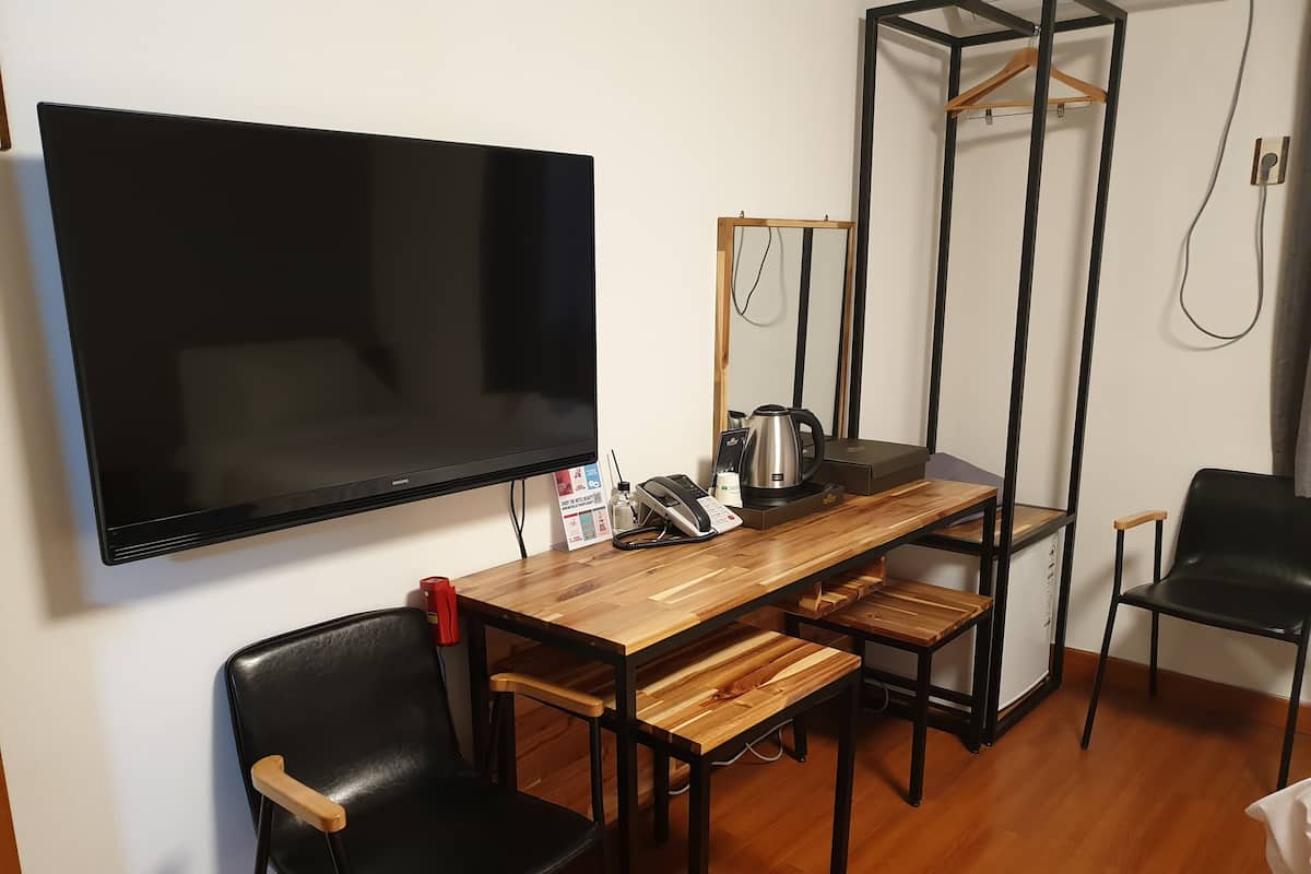 Ett litet, modernt rum med ett träbord, svarta stolar, en stor TV med platt skärm, en spegel, en vattenkokare och ett litet skåp.