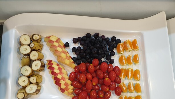 A white tray with sliced bananas, apples, blueberries, cherry tomatoes, and orange segments. - The Beauty Hotel (Gangneung)
