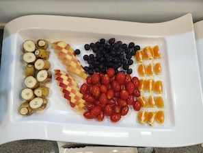 A white tray with sliced bananas, apples, blueberries, cherry tomatoes, and orange segments. - The Beauty Hotel (Gangneung)