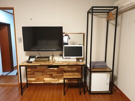 Un espacio de trabajo funcional con un escritorio de madera, un televisor de pantalla plana, un ordenador de escritorio y un refrigerador pequeño.