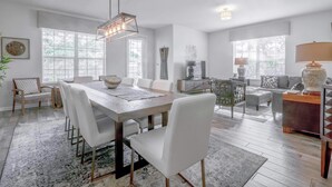 A spacious living area with a dining table, white chairs, and a sofa.