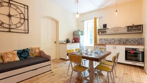 A cozy living room with a sofa, a dining table with chairs, a kitchen area with appliances, and a clock on the wall. - La Souliere (Aubin)