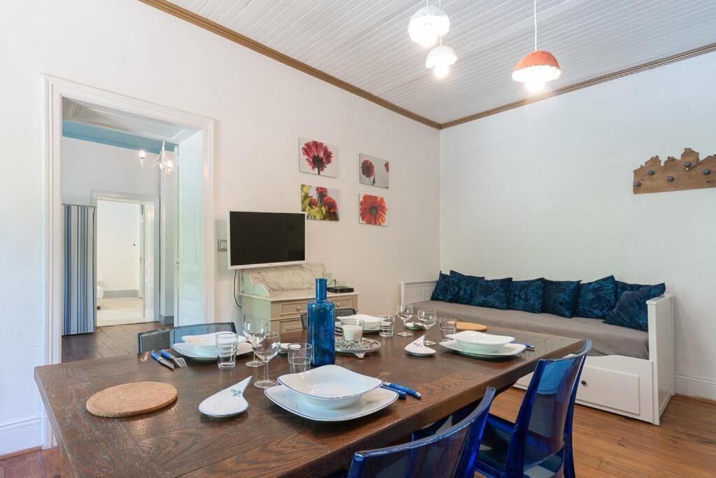 A dining area with a wooden table set for four, a sofa with blue cushions, and a television on the wall.