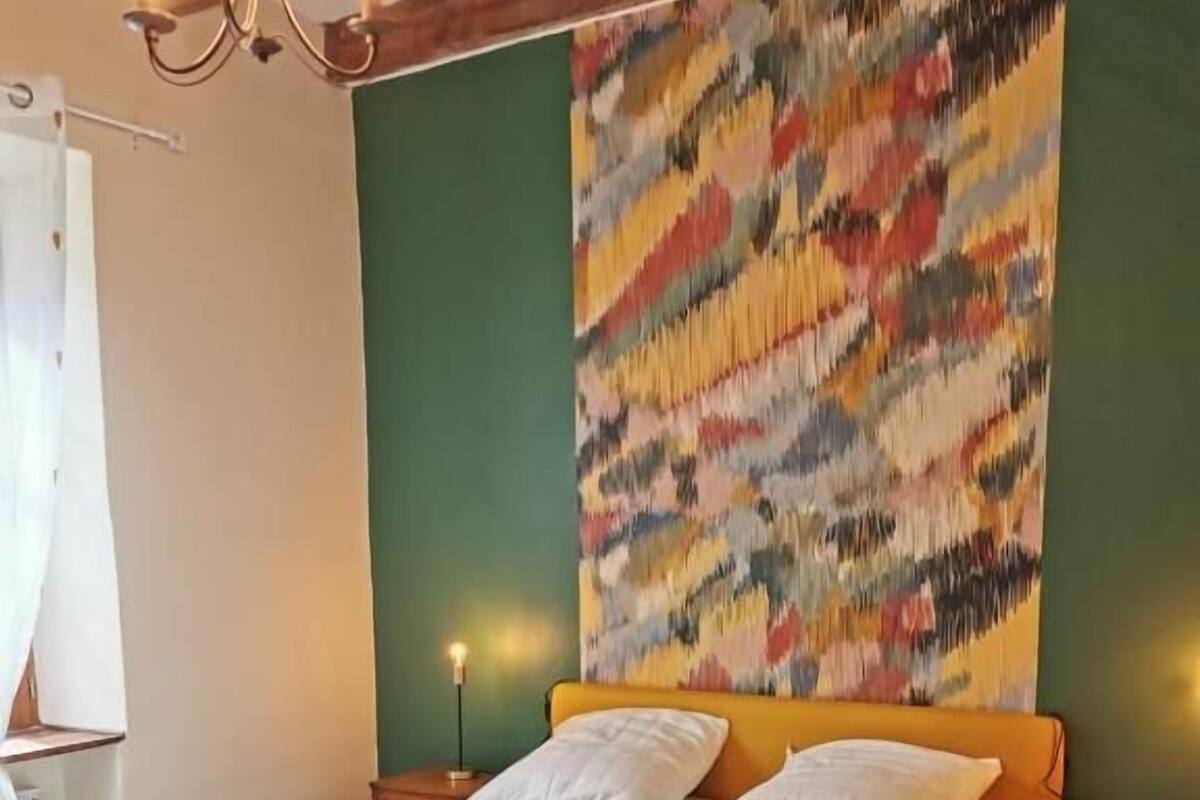 A bed with a white bedspread in a room with green walls and a colorful abstract painting above it.
