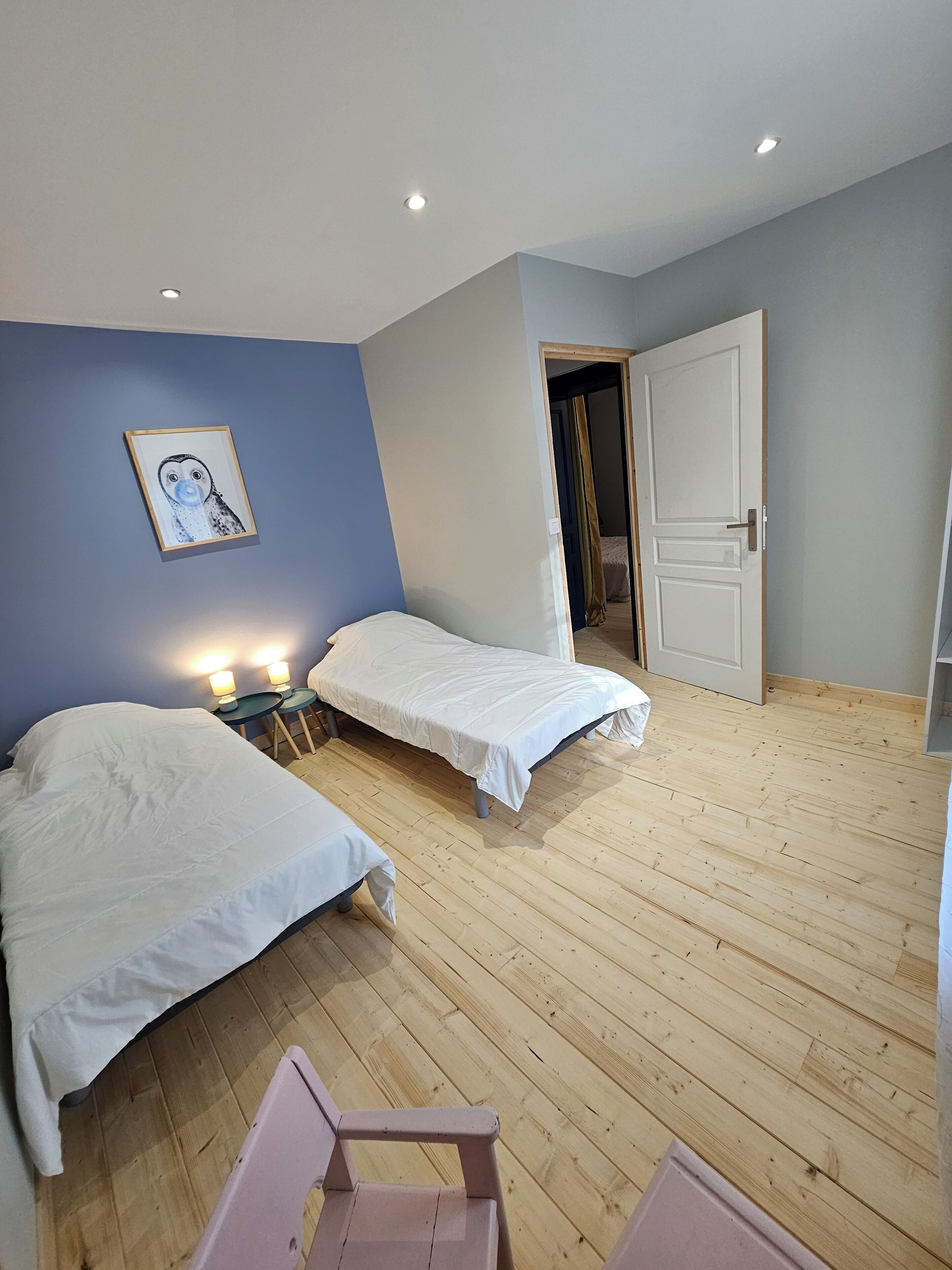 A bedroom with two single beds, wooden flooring, a framed picture on the wall, and a door leading to another room.