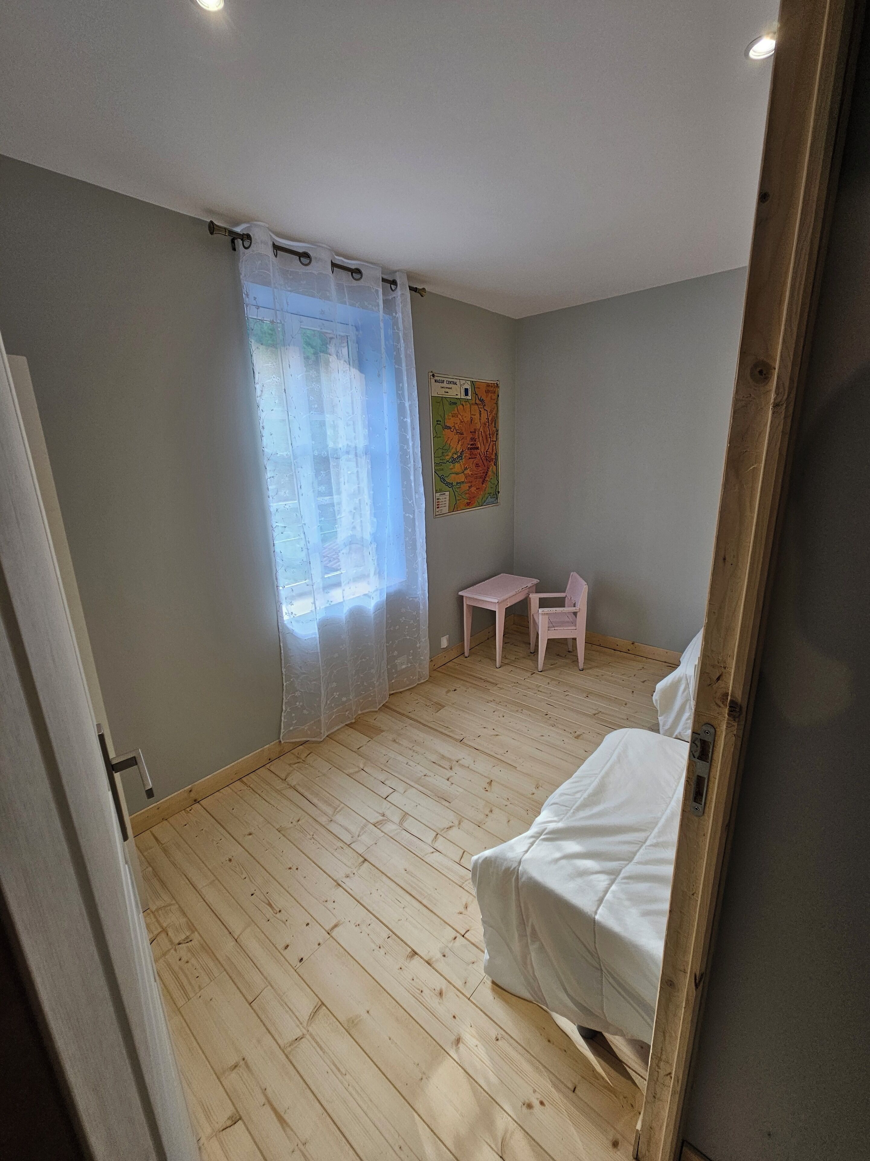 Een slaapkamer met houten vloer, een bed, een tafeltje, een stoel en een kaart aan de muur.
