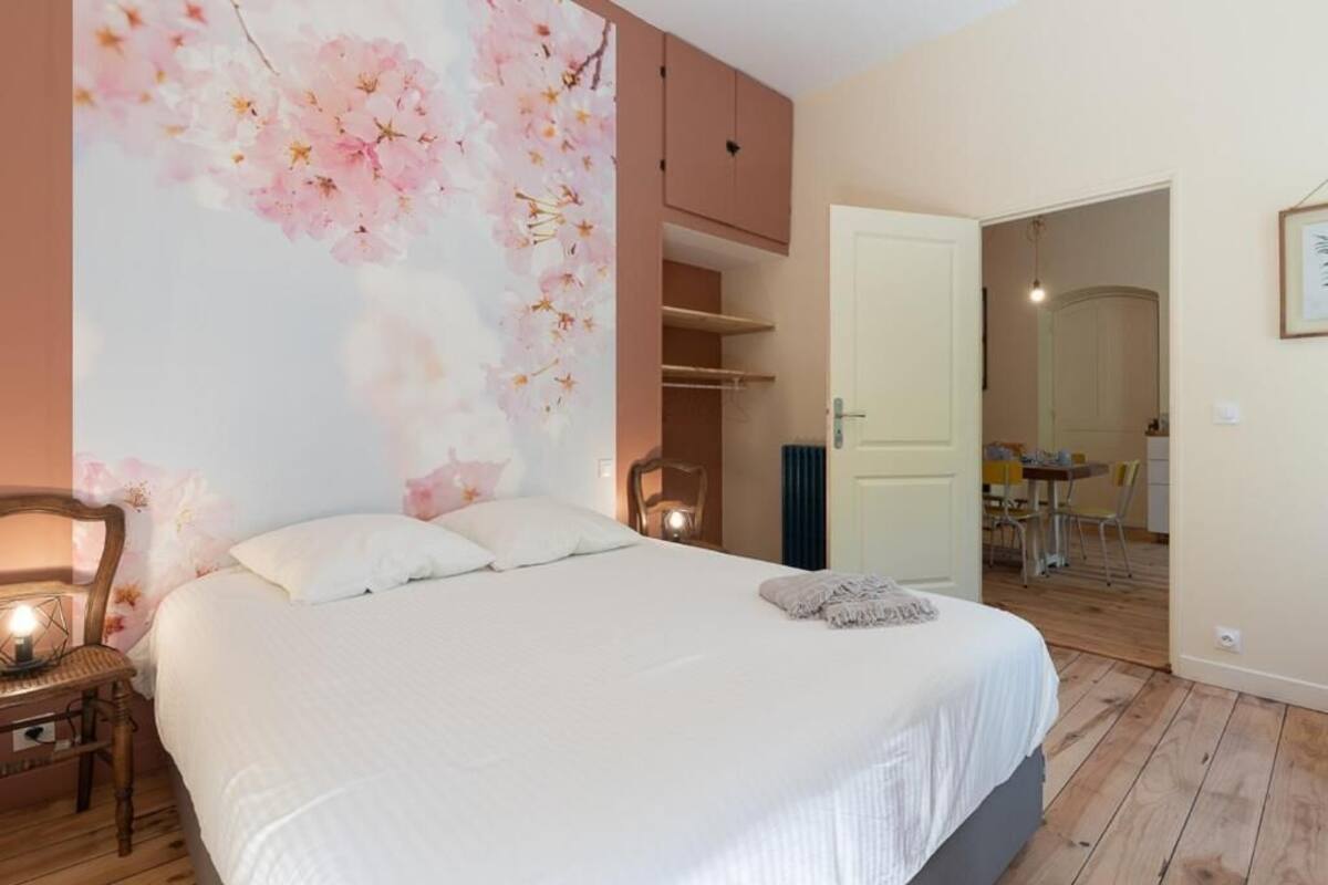 A bedroom with a large bed, a wooden chair, a wardrobe, and a door leading to a dining area.