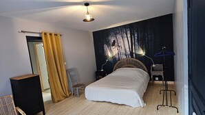 A bedroom with a bed, a chair, a small table, a wardrobe, and a wall with a forest mural. - La Souliere (Aubin)
