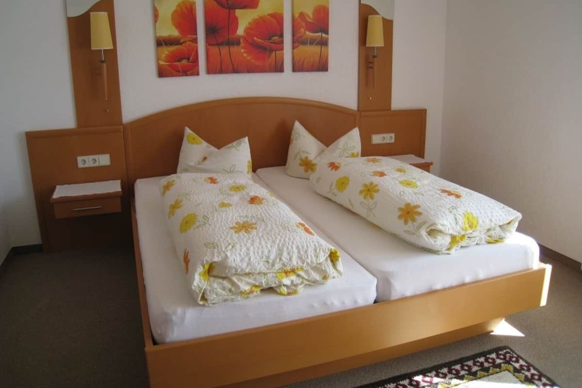 Een tweepersoonsbed met bloemenbedrukking, twee nachtkastjes en een spiegel boven het bed.
