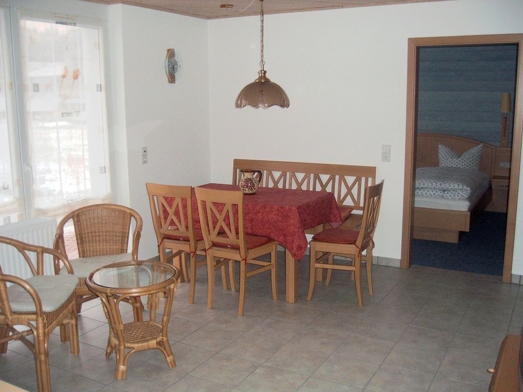 Ein Essbereich mit Tisch und Stühlen, einer Hängeleuchte und Blick in ein Schlafzimmer.