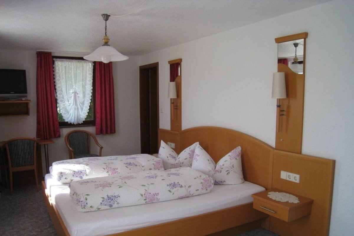 Een slaapkamer met een houten bed, een nachtkastje, een spiegel, een stoel en een televisie op een dressoir.