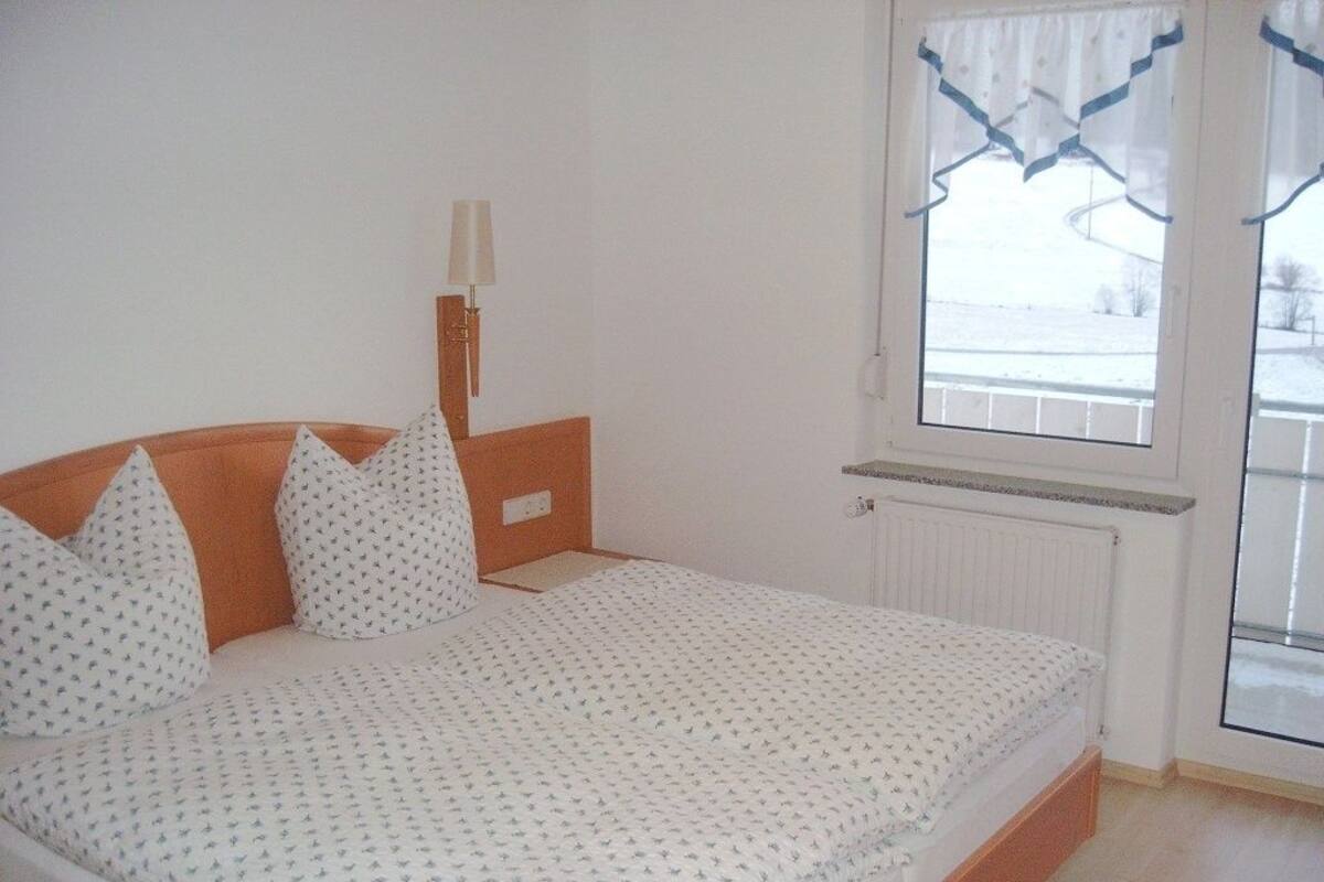 Een slaapkamer met een bed, nachtkastje, lamp en raam met gordijnen.
