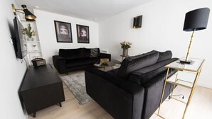 Ein modernes Wohnzimmer mit einer schwarzen Couch, einem Couchtisch und einem Fernseher auf einem Schrank.