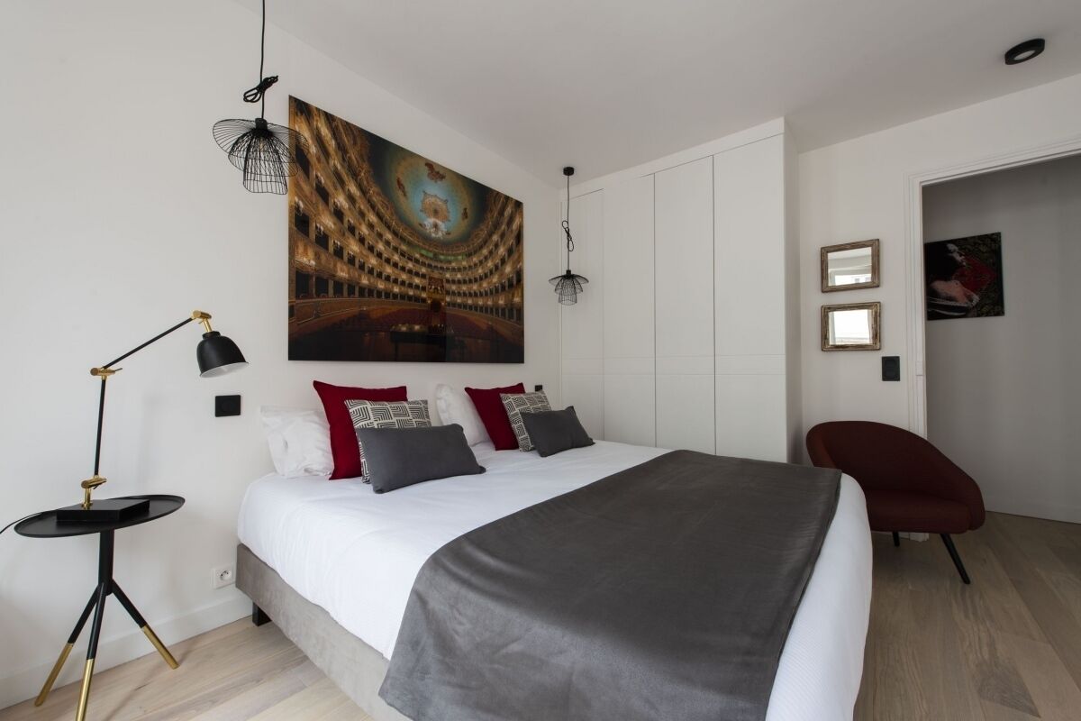 A modern bedroom with a large bed, a standing lamp, a chair, and a painting on the wall.