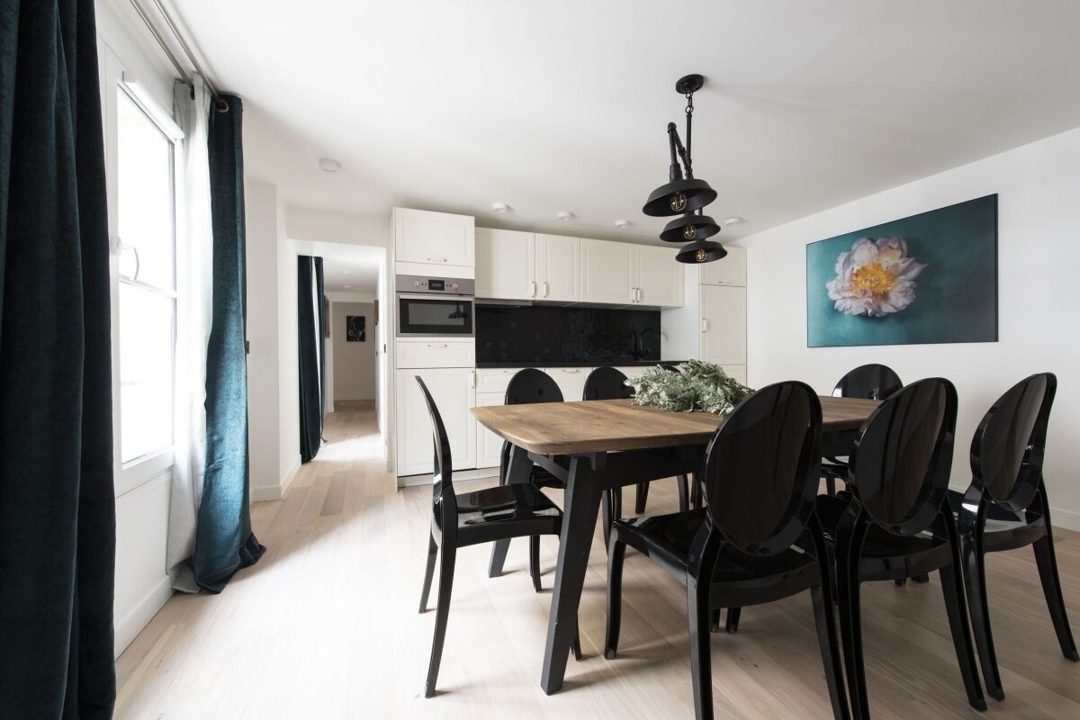 Una cocina moderna con armarios blancos, encimera negra y una mesa de comedor de madera con sillas negras.
