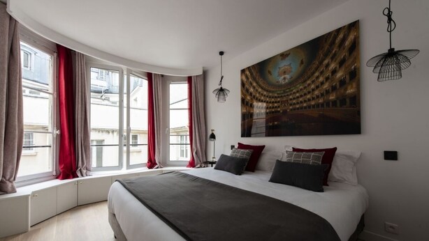 Ein Schlafzimmer mit einem großen Bett, einem gebogenen Fenster, einem Stadtbildgemälde und einer Pendelleuchte.