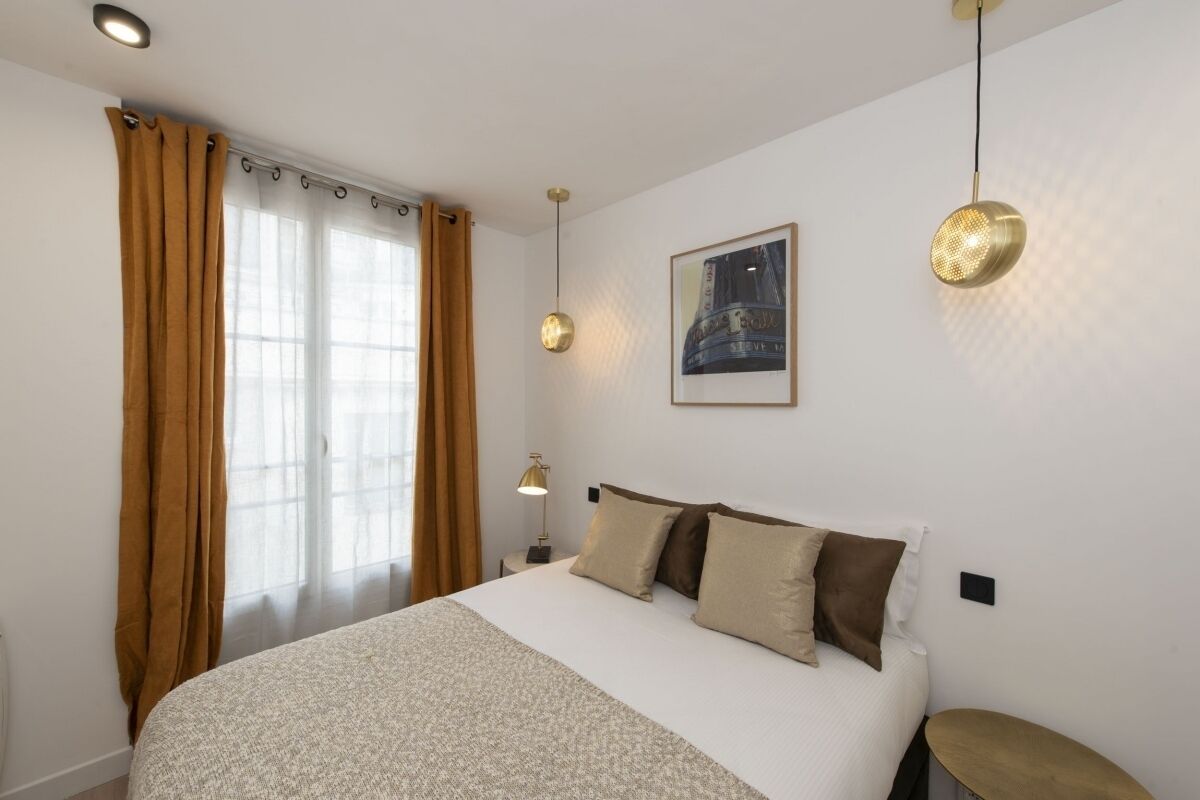 A hotel room with a large bed, a bedside table, a lamp, and a window with curtains.