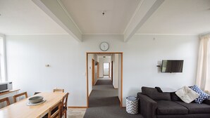 A modern living room with a dark grey sofa, a wooden dining table, and a television mounted on the wall. - Kowhai Flat (Owaka)