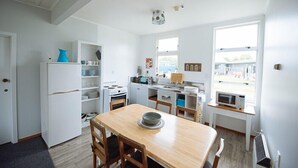 A compact kitchen with white appliances, a dining table, and a view through the window. - Kowhai Flat (Owaka)