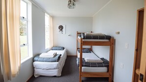 A room with bunk beds, a window with curtains, a ceiling light fixture, and a framed picture on the wall. - Kowhai Flat (Owaka)