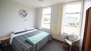 A bedroom with a bed, a chair, a window, and a wall decoration. - Kowhai Flat (Owaka)