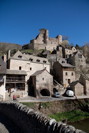 Ein historisches Steinhaus mit mehreren Ebenen und einem markanten Turm, am Fluss gelegen.