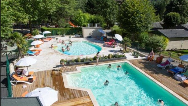 Ein Poolbereich mit mehreren Pools, Liegestühlen, Sonnenschirmen und einer Holzterrasse.