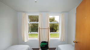 Een kamer met twee eenpersoonsbedden, een houten deur en een raam met gordijnen.