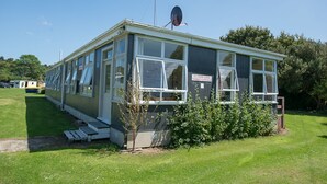 Een klein, laag gebouw met een plat dak, grote ramen en een bord waarop staat dat het een vakantieappartement is.