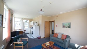 Een woonkamer met een bank, een salontafel en een televisie. Er is een keuken met een koelkast en een magnetron.