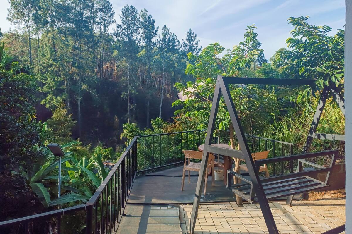 A wooden deck with a swing set, surrounded by lush greenery and tall trees.