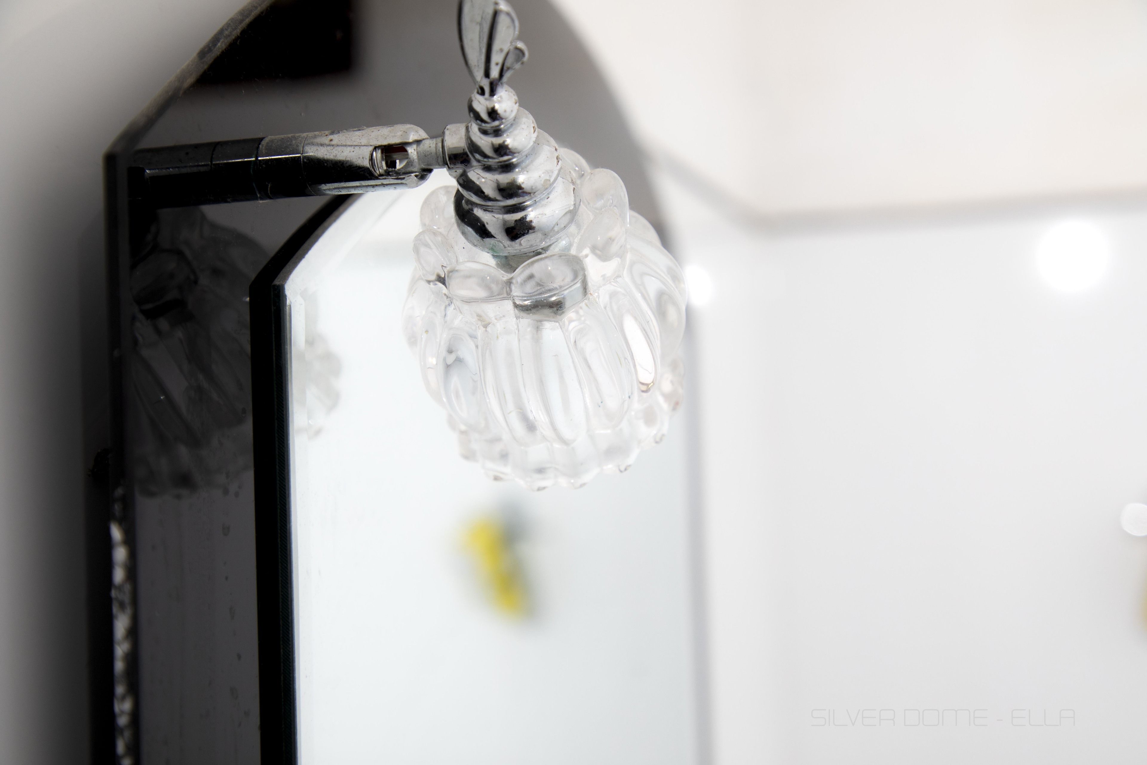 A clear glass light fixture with a metallic base, attached to a wall.
