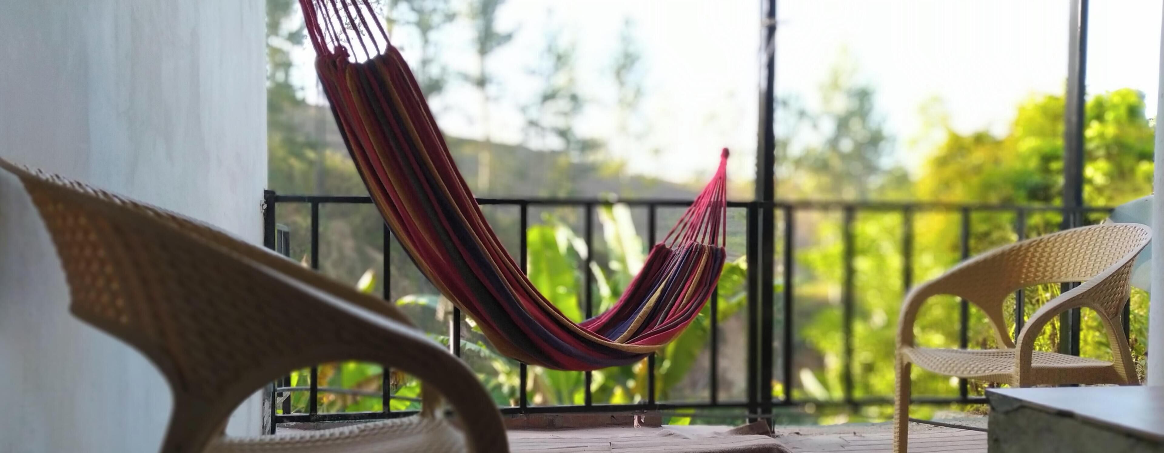 A hammock on a balcony with wicker chairs and a view of greenery.
