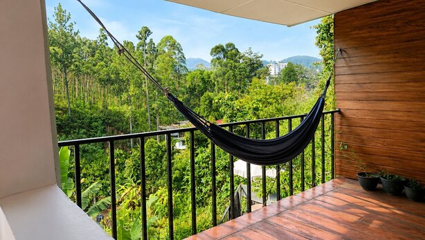 Un balcon avec un hamac, un plancher en bois et une vue sur une forêt verdoyante.