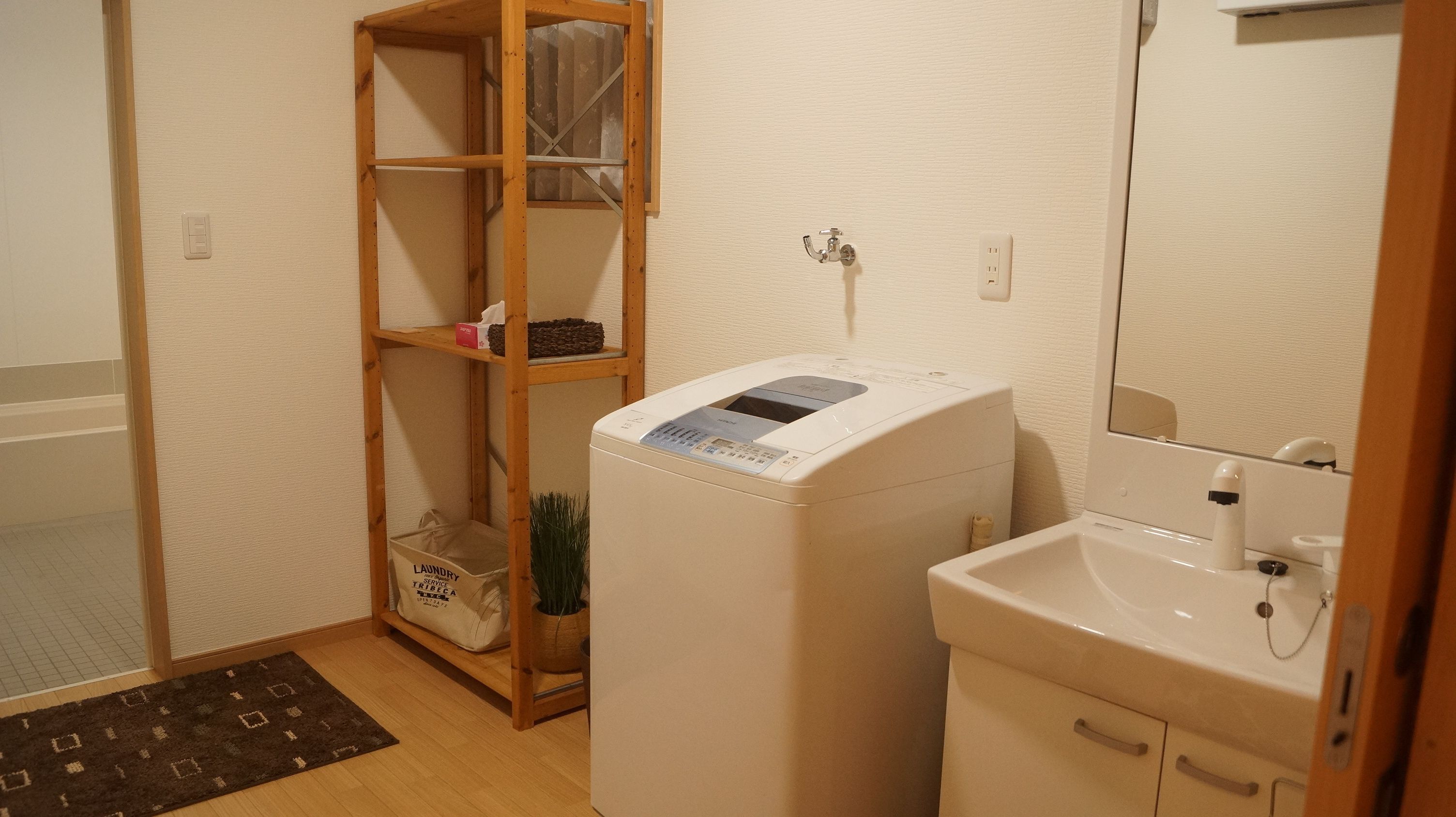 A laundry room with a washing machine, a shelf with a basket, and a sink.