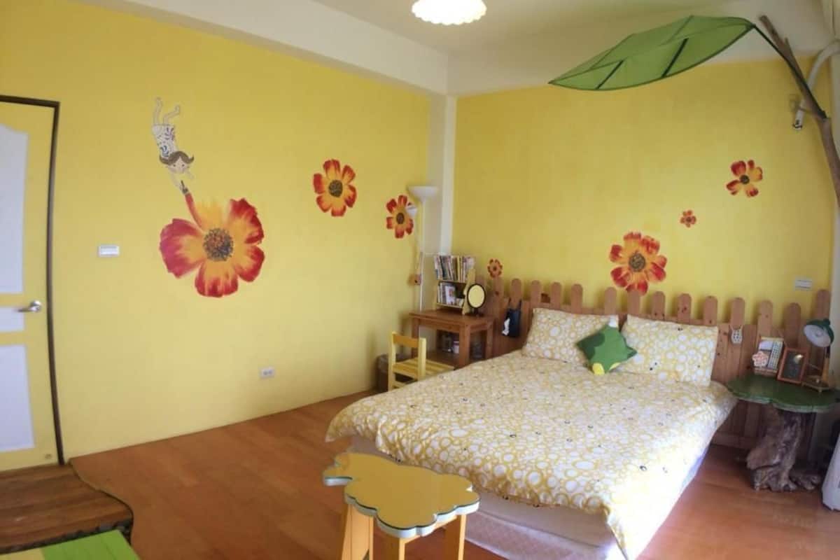 Quarto com cama, cabeceira de madeira, mesa de cabeceira, cadeira e uma pequena mesa com abajur.