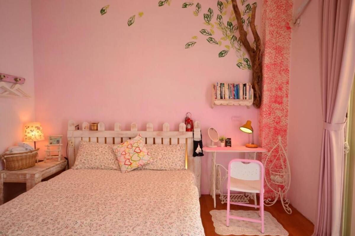 Quarto em tons de rosa com uma cama, uma escrivaninha e uma cadeira.