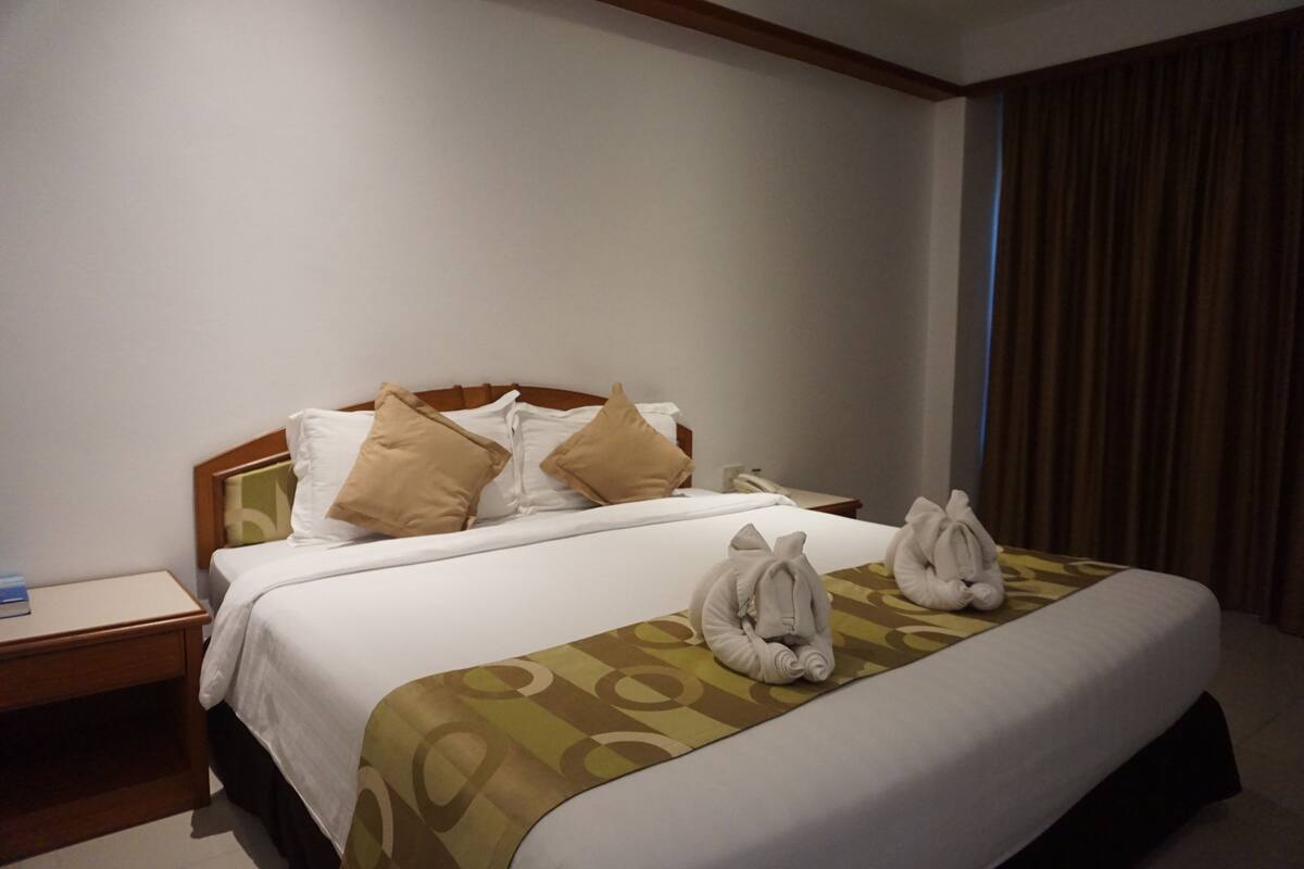 Een hotelkamer met een net opgemaakt bed, een nachtkastje met een lamp en een raam met gordijnen.