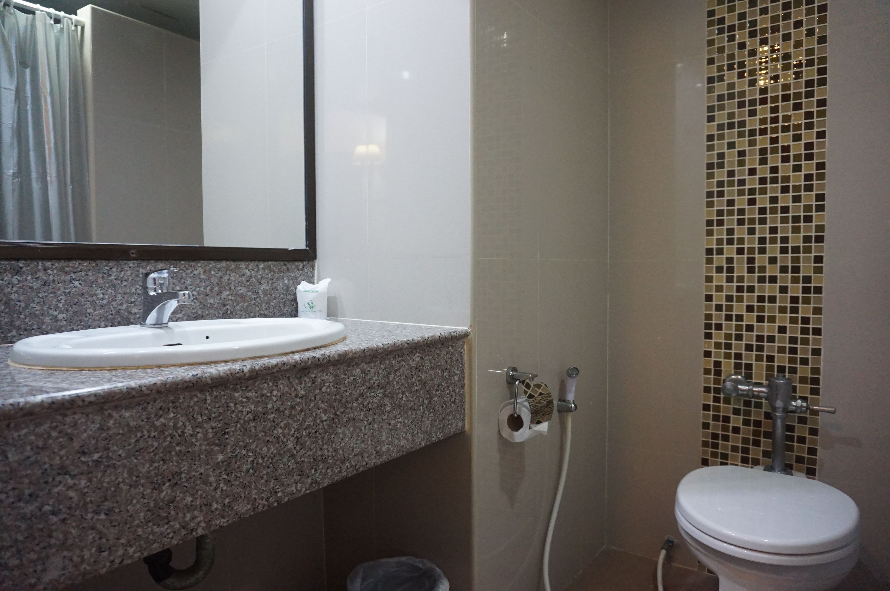 Un baño con lavamanos de encimera de granito, un espejo, inodoro y zona de ducha con mosaicos.