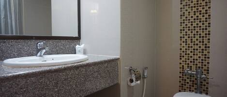 A bathroom with a granite countertop sink, a mirror, a toilet, and a shower area with mosaic tiles.