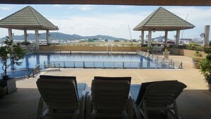 A pool area with two gazebos, lounge chairs, and a view of distant mountains. - Green World Palace Hotel (Songkhla)