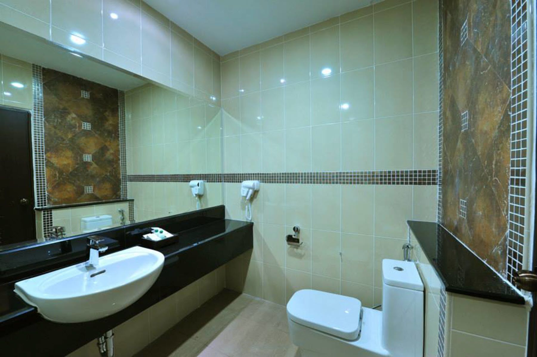 A modern bathroom with a large mirror, a black countertop, a white sink, a toilet, and a hand dryer.