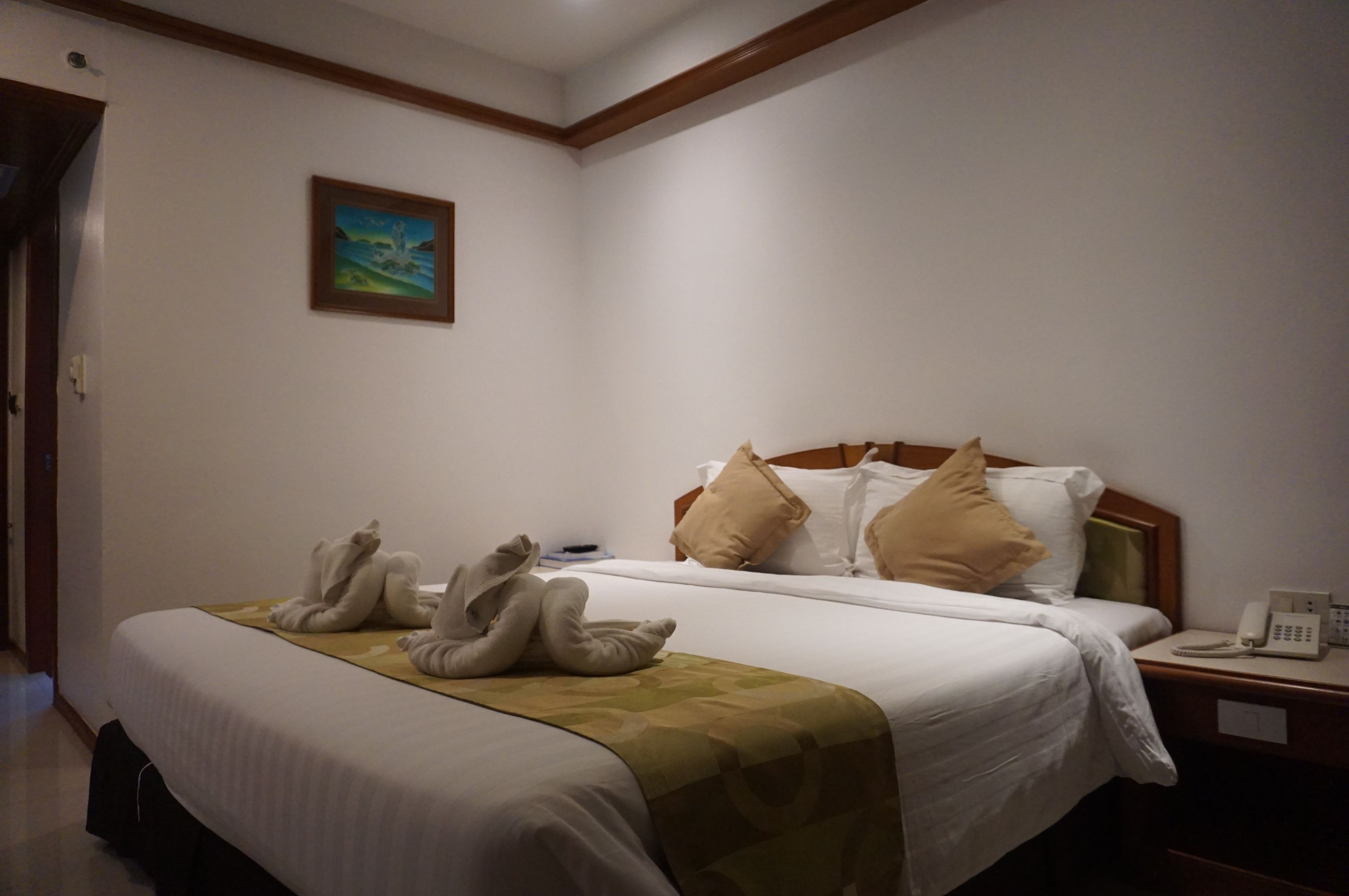 A hotel room with a neatly made bed, a painting on the wall, and a telephone on the nightstand.